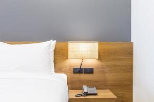 primer plano de la almohada blanca en la decoración de la cama con lámpara de luz y teléfono digital en el interior de la habitación del hotel. foto