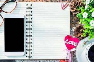 Top view image of empty notebook,smartphone,spectacles and cup of coffee on Marble floor background. Love concept with heart desktop,Valentine's Day. photo