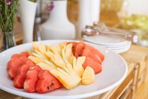 Chop the pieces of watermelon and pineapple in white dish the dining and flower vase on table decorationat buffet self service at hotel. photo