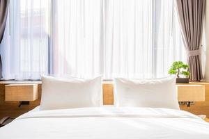 Close-up of white pillow on bed decoration with light lamp and green tree in flowerpots in hotel bedroom interior. photo