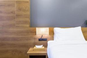 Close-up of white pillow on bed decoration with light lamp and tissue box in hotel bedroom interior. photo