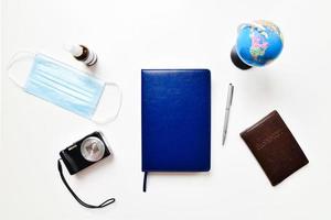 Flat lay with copy space, working from home concept during the Covid-19 pandemic. A smart phone, sunglasses, laptop, shoes, passport, a face mask and notepad arranged on white table background photo