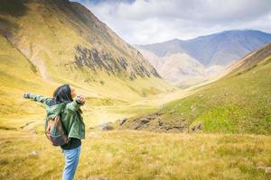 mochilero femenino se encuentra en la roca y disfruta de impresionantes vistas de las montañas en el valle de juta. exploración del parque nacional kazbegi foto