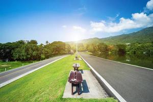 Dos sillas sentadas en la hierba verde y a lo largo de la vista del paisaje de la carretera en la universidad ang kaew chiang mai montaña boscosa fondo de cielo azul con nubes blancas foto