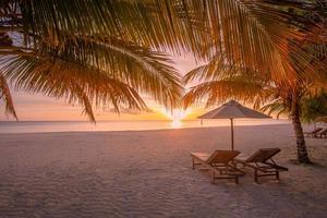 hermoso paisaje de puesta de sol tropical, dos hamacas, tumbonas, sombrilla debajo de una palmera. arena blanca, vista al mar con horizonte, cielo crepuscular colorido, tranquilidad y relajación. hotel de resort de playa inspirador foto