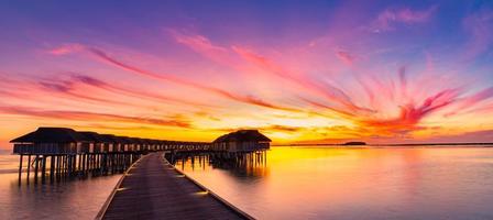 Sunset on Maldives island, luxury water villas resort and wooden pier. Beautiful sky and clouds and beach background for summer vacation holiday and travel concept photo