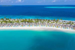 Aerial view of Maldives island, luxury water villas resort and wooden pier. Stunning sky and ocean lagoon beach. Summer vacation holiday and travel concept. Paradise aerial landscape panorama photo