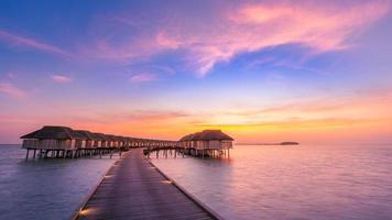 increíble panorama de la puesta de sol en maldivas. Villas de resort de lujo marino con luces LED suaves bajo un cielo de colores. hermoso cielo crepuscular y nubes de colores. hermoso fondo de playa para vacaciones vacaciones foto