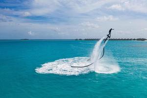 Aerial view of water extreme action sport, summer sea, close to luxury tropical resort . Fly board in ocean lagoon, freedom fun as summer recreational activity. Flyboard view from drone photo