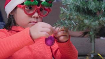 petite fille au bonnet de noel décore l'arbre de noël à l'intérieur. Bonne année et joyeux Noël.