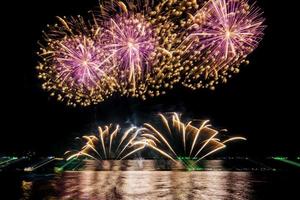 Increíble y hermoso colorido espectáculo de fuegos artificiales en la noche de celebración, que se muestra en la playa del mar con reflejos multicolores sobre el agua foto