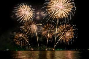 Increíble y hermoso colorido espectáculo de fuegos artificiales en la noche de celebración, que se muestra en la playa del mar con reflejos multicolores sobre el agua foto