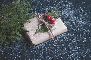 Christmas gift box made of kraft paper with snow on a black table with fir branches. photo