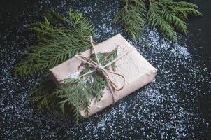 One gift is wrapped in kraft paper with fir sprigs on a black board.