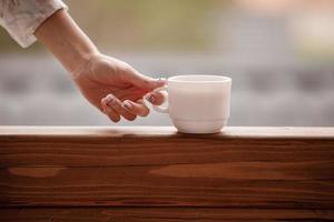 Morning coffee cup. Female hand holds white cup of morning hot drink - coffee or tea on the balcony on the background of mountain nature. photo
