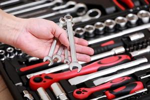 Tool store. Closeup of male hand holding wrenches. Auto repair kit in toolbox. Repairman instruments set. Inside the toolbox there are black-red wrenches, spanners and different nozzles. Closeup. photo