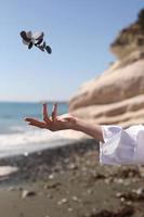 female hand throws a pebble in her hand against the background of the blue sky, beach, rock and sea. photo