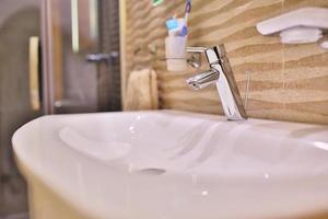 Luxury faucet mixer on a white sink in a beautiful gray interior bathroom. close up view of nice metal faucet in modern bathroom. photo