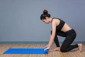 Young asian woman preparing yoga mat for practicing yoga at yoga healthy sport gym. Yoga and meditation have good benefits for health. Photo concept for Yoga Sport and Healthy lifestyle.