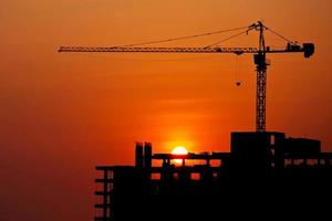 Silhouetted construction crane and building at construction site on sunset for construction industrial work concept photo