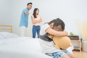 Niña asiática tristeza mientras los padres pelean en el dormitorio.Diseño de fotos para problemas familiares y concepto infeliz.