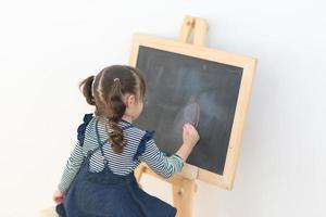 Happy asian girl kid draw cartoon with chalk on blackboard for learning at home. Photo for kid education and school study concept.