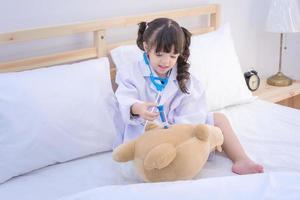 Cute asian little girl enjoy playing doctor with doctor toy set and cute doll at home.Photo design for family, kids and happy people concept.