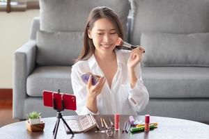 Influencer de belleza femenina asiática haciendo un video tutorial para su canal de belleza sobre cosméticos durante la estancia segura en casa foto