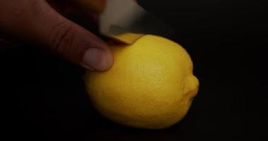 De cerca, la mano del chef utiliza un cuchillo para cortar limones. cortar el limón por la mitad. sobre el fondo negro. video