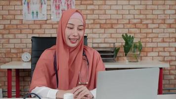 retrato de uma linda médica, linda muçulmana de uniforme com estetoscópio, sorrindo por videochamada com laptop na clínica do hospital. uma pessoa com experiência em tratamento profissional. video