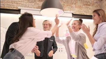 geluk jonge multiraciale collega's team viert zakelijk succes met blanke baas door papieren te gooien en te klappen, opgewekt wanneer de vergadering eindigt in de conferentiewerkplek van een kantoor. video