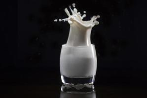 chorrito de leche del vaso sobre un fondo negro foto
