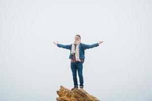 Traveler man with a backpack standing on top of mountain top with hands raised in air photo