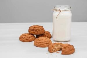 Milk in a glass jar and oatmeal cookies on a white table background. Copy, empty space for text photo