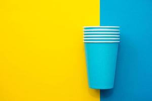 Blue paper disposable cups yellow and blue background. Cooking utensil. Cutlery sign. Top view. Minimalist Style. Copy, empty space for text photo