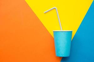 Blue paper cups with drinking colored plastic straws on beautiful multicolored background. Set for party. Top view. Minimalist Style. Copy, empty space for text photo