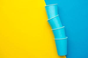 Blue paper disposable cups yellow and blue background. Cooking utensil. Cutlery sign. Top view. Minimalist Style. Copy, empty space for text photo