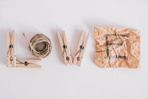Inscription word love made of wooden clothespins, rope and brown paper sticker on white background. View from above. Place for your text photo