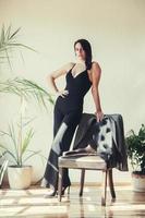 Woman dressed in black clothes standing near armchair in loft style interior photo