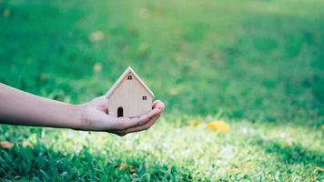 mano sosteniendo el modelo de la casa en el fondo de la naturaleza, ahorrando dinero en casa o préstamo para planificar la inversión empresarial por concepto de bienes raíces. foto