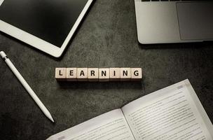 Blank screen tablet, pen, laptop, textbook and word learning on wood cube block on black table background photo