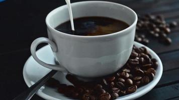 o creme é derramado em uma xícara de café expresso e grãos de café em um fundo de madeira.