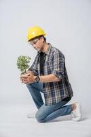 A man wears orange gloves and sit to hold a plant pot in the house. photo