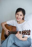 The girl sat and played the guitar on the bed. photo