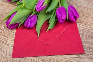 Sobre rojo con tulipanes sobre una mesa foto