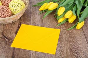 Sobre amarillo con tulipanes sobre una mesa foto