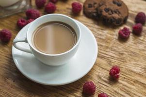 Taza de café blanco con galletas de chocolate frambuesas fondo de madera foto