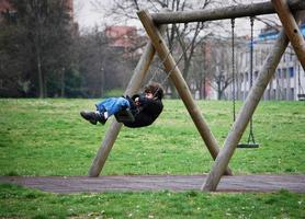 Bologna, Italy, 2019 - Child plays alone on a swing in the park playground. photo