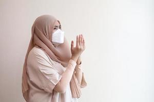 Muslim Girl wearing a surgical mask praying during work from home. Covid-19 coronavirus concept. photo