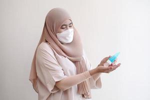 Mujer musulmana con una mascarilla quirúrgica lavándose las manos con gel de alcohol sobre fondo pastel. concepto de coronavirus covid-19.